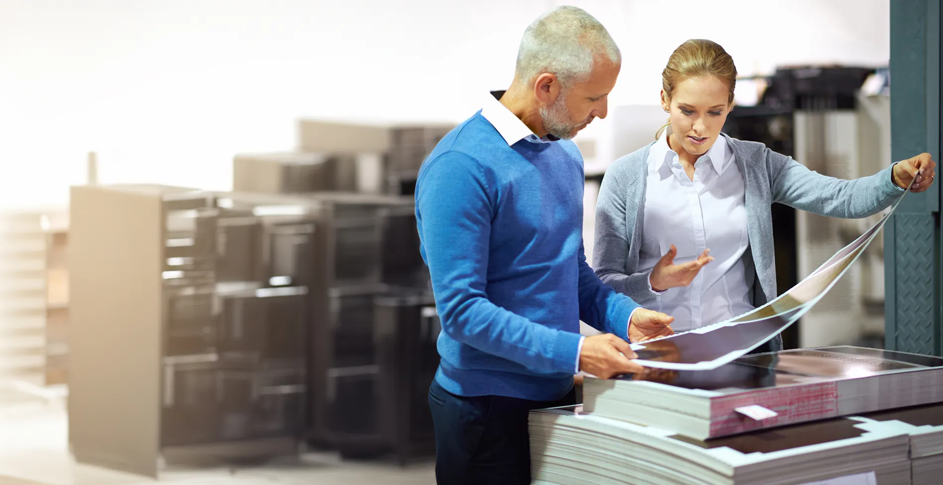 a man and woman in a printing shop looking at large prints 